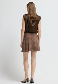Top en satin marron avec une ouverture en clé au dos, associé à une jupe plissée texturée marron et beige. Porté avec des chaussures à talons noirs.