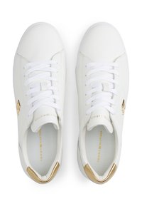 Biele kožené tenisky s plochými bielymi šnúrkami, zlatými doplnkami na päte a logu, textúrovaným vnútrom a hladkým povrchom.
