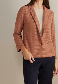 Texturovaný blejzr v růžové barvě s jedním knoflíkem a klopovým límcem. Má tříčtvrteční rukávy a boxy střih.