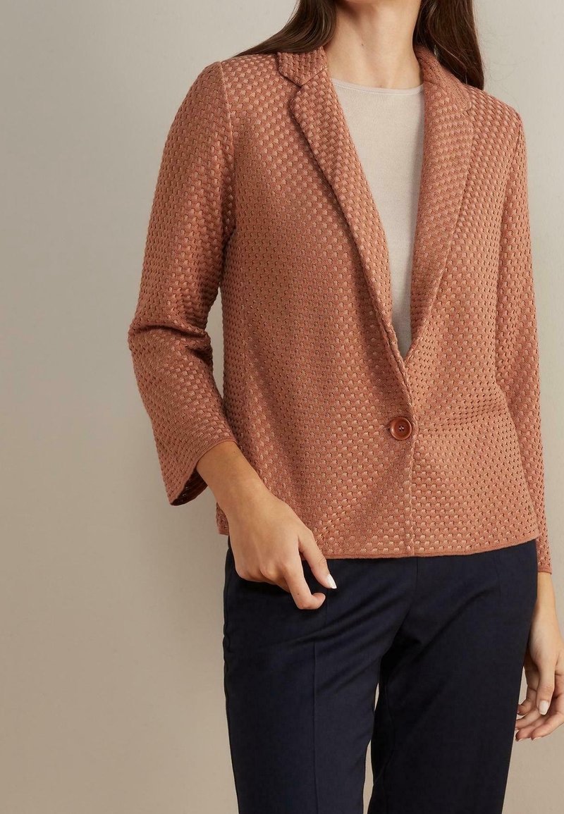 Texturovaný blejzr v růžové barvě s jedním knoflíkem a klopovým límcem. Má tříčtvrteční rukávy a boxy střih.