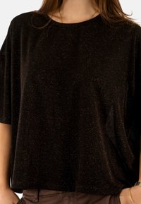 Top negro de manga corta con un corte relajado, que presenta una superficie texturizada con pequeñas motas metálicas para un efecto de brillo sutil.
