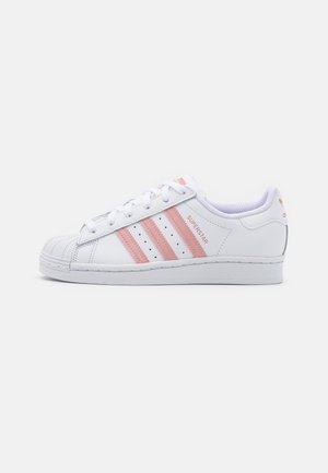 Baskets basses Adidas Superstar blanches avec des bandes roses, des lacets roses, un bout renforcé et le texte "Superstar" sur le côté.