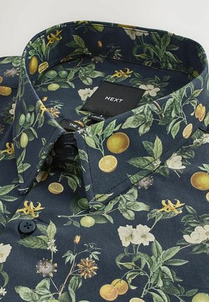 Chemise pour homme avec un fond bleu foncé et un motif floral et de fruits d'agrumes. Fabriquée dans un tissu à texture lisse et avec un col boutonné.