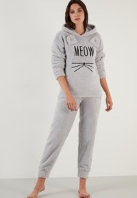 Sivi, pahuljasti pidžama set koji uključuje kapu s ušima, otisak "MEOW" i dizajn mačjih brkova. Mekana tekstura, opušteni kroj s pijanim hlačama.