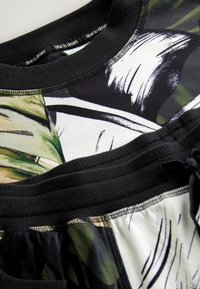 Sweatshirt multicolore avec des accents noirs, un col côtelé et des motifs abstraits de feuilles en vert, beige et blanc. Taille ajustable.