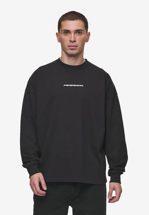 Sort oversized sweatshirt med lange ærmer, rund hals og hvid logo detalje centreret på brystet. Glat bomuldsstof.