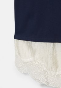 Ourlet en tissu bleu marine avec un matériau blanc froissé superposé en dessous, présentant une bordure en dentelle florale détaillée le long du bord.