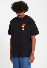 Black cotton t-shirt featuring a colorful graphic design on the left chest with red, orange, and yellow elements. Relaxed fit, short sleeves.