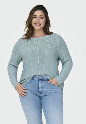 Pull en tricot bleu clair, avec un col rond, des manches longues et des fentes sur les côtés, associé à un jean bleu clair.