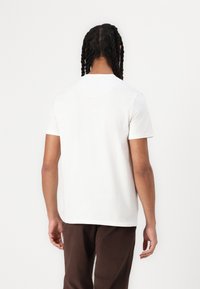 Tricou alb din bumbac, cu mâneci scurte, gât rotund și o croială lejeră. Cusături vizibile de-a lungul marginii și o textură netedă.