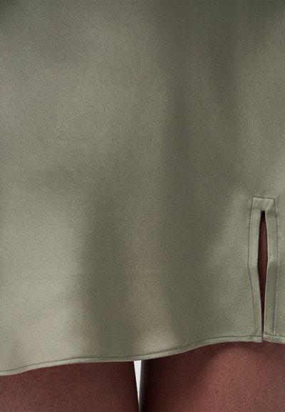 Κοντινό πλάνο κάτω μέρους φούστας ελιάς με μικρή πλαϊνή σχισμή που δείχνει σκούρο δέρμα από κάτω.