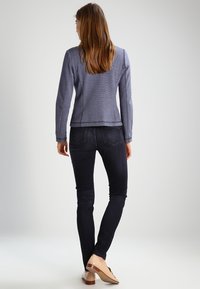 Ljust blå texturerad jacka, figursydd design, ihopparad med mörka skinny jeans och beige skor. Bakifrån visas enkel sömnad och sömlig fåll.