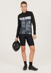 Långärmad cykeltröja i svart och grått med dragkedja och abstrakt mönster, matchad med svarta shorts och hjälm, i lättviktig tyg.