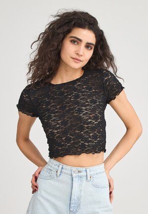 Crop top in pizzo nero con scollatura rotonda, maniche corte, bordi spellonati e motivo floreale, abbinato a pantaloni corti in denim chiaro a vita alta.