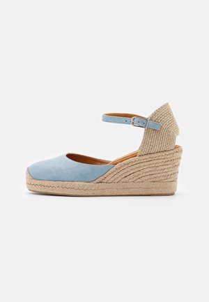 Sandale à compensée en daim bleu avec une bride autour de la cheville, un talon enveloppé de jute et des accents tissés à l'arrière. Bout arrondi et semelle intérieure rembourrée.