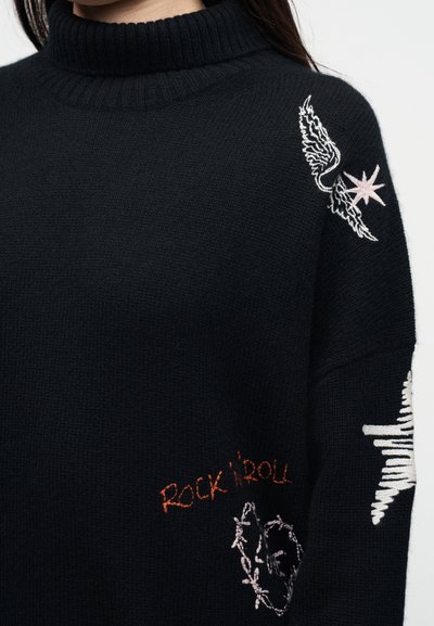 Pull noir à col roulé avec une aile brodée, une étoile, le texte « ROCK 'N' ROLL » et des motifs d'onde sonore sur l'épaule et la manche.