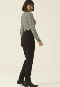 Pantalons noirs ajustés associés à un haut à rayures noir et blanc à manches longues, avec un col rond et un tissu lisse.