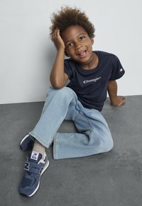 T-shirt bleu Champion avec logo, jean bleu clair et baskets navy. La texture comprend un tissu doux et des accents en maille sur les chaussures.