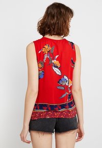 Czerwona top bez rękawów z haftem kwiatowym w kolorze niebieskim, żółtym i zielonym, z wzorzystym dołem w granatowo-czerwonym. Miękka, teksturowana tkanina.