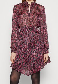 Abito nero a fiori con maniche lunghe, texture plissettata e orlo a volant. Presenta fantasie di fiori rosa e viola e un collo a chiave.