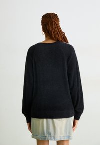 Sweater preto oversized com mangas longas, feito de um material macio e texturado. Combinado com uma saia de ganga clara. Design minimalista, sem padrões.