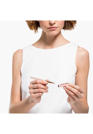 Applicateur de maquillage en or rose avec prise décorative, tenu d'une main tandis qu'un capuchon cylindrique rose est tenu de l'autre. Finition métallique et lisse.