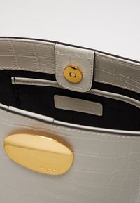 Interno di borsa in pelle effetto coccodrillo grigia, con chiusura circolare dorata, fodera nera e etichetta che indica il materiale in pelle.