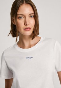 Biela bavlnená tričko s okrúhlym výstrihom a krátkymi rukávmi, s malým modrým logom "PEPE JEANS LONDON" na hrudi.