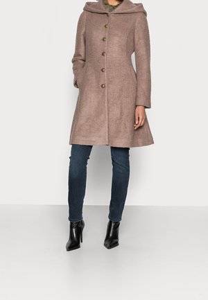 Mujer con abrigo de lana color malva en línea A con capucha y botones de latón, vaqueros azul oscuro y botines de cuero negros.