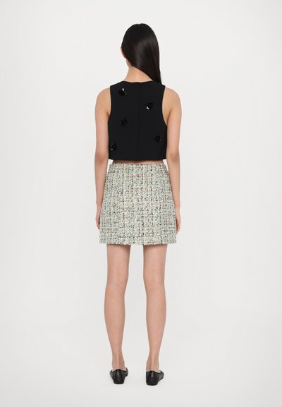 Black crop top with decorative black flowers, paired with a textured pastel tweed skirt. The outfit features a fitted silhouette.