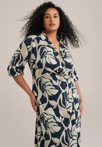 Bloemendess jurk met marineblauw en crème kleuren, met een v-hals, driekwart mouwen en een wikkelontwerp. Getextureerde stof.