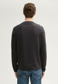 Camisa de manga larga gris oscuro con cuello redondo, hecha de una tela suave. Presenta una silueta ajustada y un dobladillo recto. Se lleva con jeans de mezclilla azul.