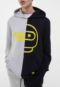 Färgblockerad huvtröja i grått och marinblått, med gula grafiska tryck. Material: mjuk bomullsblandning, med en känguruficka.