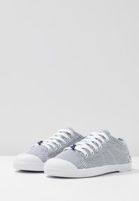 Sneakers in tela con strisce blu navy e bianche, punta in gomma bianca e lacci. Forma arrotondata con tessuto testurizzato e branding minimal.