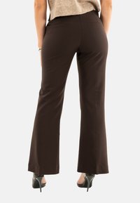 Pantaloni a palazzo marroni con una texture liscia, caratterizzati da una vita alta, tasche posteriori e abbinati a scarpe con tacco nere.