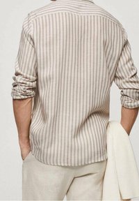 Chemise beige clair à manches longues avec des rayures verticales étroites dans des teintes plus foncées. Tissu doux avec manches retroussées et coupe décontractée.