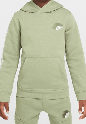 Barn iført en lysegrøn Nike-hættetrøje og matchende bukser med hvide Nike-logoer på brystet, venstre ben og ærme.