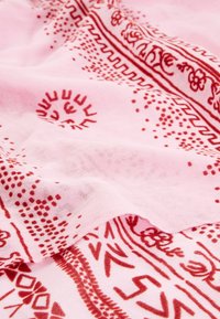 Tissu rose doux avec des motifs floraux et géométriques rouges complexes, présenté avec des plis doux et une texture.