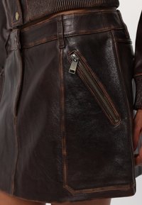 Gonna in pelle marrone con una superficie liscia, caratterizzata da una tasca con zip diagonale, cuciture a vista e un design strutturato.
