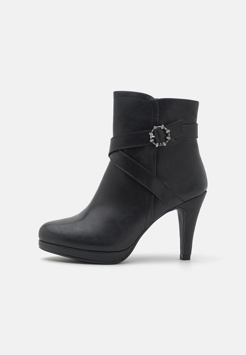 Bota negra de tobillo hecha de cuero sintético con punta afilada, tacón alto y correa decorativa con un detalle metálico circular.