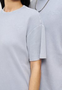 Κοντινό πλάνο δύο ατόμων που φορούν μπλουζάκια με κοντά μανίκια και πλέξη βάφλ σε ανοιχτό μπλε χρώμα, το ένα με ασημένιο κολιέ αλυσίδα.