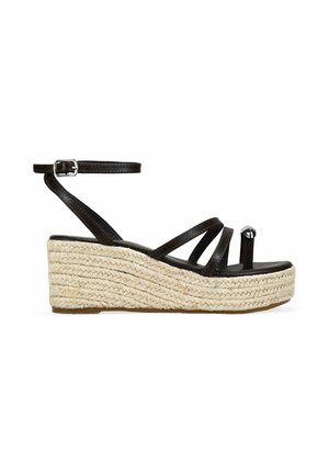Sandalia negra de piel con cuña, con correa en el tobillo y suela plataforma trenzada de yute, con lazo para el dedo y hebilla plateada.