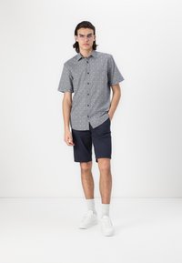 Cămașă cu mânecă scurtă, cu un model albastru, cu nasturi în față, purtată cu pantaloni scurți bleumarin și adidași albi. Material fin, croială lejeră.