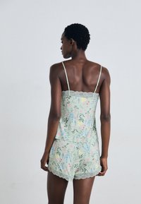 Lichtgroene bloemenpatroon camisole met kantafwerking en bijpassende shorts. Voorzien van verstelbare schouderbandjes en golvende randen. Zachte stof.