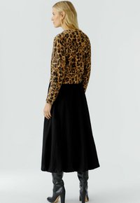 Lepelprint cropped fuzzy trui gecombineerd met een lange zwarte rok en hoge grijze laarzen, wat een elegante silhouet en textuurcontrast toont.