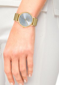Goldmesh-Armbanduhr mit einem runden silber-blauen Ziffernblatt, minimalistische Stundenmarkierungen und einem kleinen Datumsfenster auf der 6-Uhr-Position.