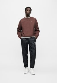 Μπορντό φούτερ με γκρι γιακά, μακριά μανίκια; μαύρο κωνικό παντελόνι με ελαστικά τελειώματα, λογότυπο Nike; λευκά αθλητικά παπούτσια.