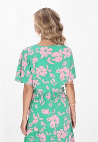 Abito floreale con una base verde e grandi fiori rosa, maniche corte, vita arricciata e orlo inferiore a strati.