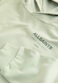 Lysegrøn hættetrøje med ribbet manchet og teksten "ALLSAINTS LONDON", inklusive japanske tegn, trykt på brystet.
