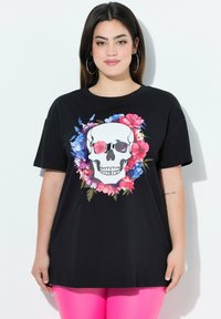 Sort bomulds t-shirt med et stort kraniegrafik indrammet af levende blomsterdesigns i pink, blå og grøn. Korte ærmer, afslappet pasform.